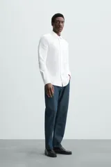 Camisa celeste a rayas verticales blancas, de corte recto, con cuello italiano abierto, mangas largas con puños abotonados y cierre frontal con botones.
