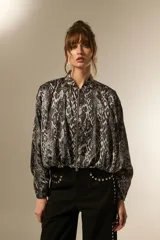 Campera estilo bomber de manga larga, con cuello mao y cierre frontal. Confeccionada en tejido de poliéster con estampado de piel de serpiente en tonos grises y negros.