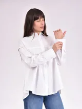 Camisa blanca de corte clásico, con cuello camisero, cierre frontal con botones y mangas largas con puños abotonados.