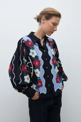 Camisa de manga larga, color azul marino, con estampado floral en tonos rojo, blanco y celeste. Presenta un diseño frontal con paneles ondulados en color celeste claro.