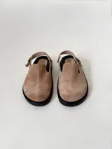 Zuecos color beige de cuero gamuzado, con punta cerrada, suela de goma negra y tira trasera con hebilla metálica.