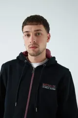 Campera marrón de felpa con capucha y cordón ajustable, lettering estampado en la espalda, bolsillo en la manga, puños y logo en grifa de goma.