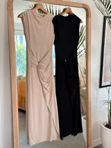 Vestido largo negro, sin mangas, con cuello drapeado y detalle de nudo fruncido con hebilla metálica en la cintura. Presenta una abertura alta en la falda.