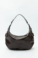 Cartera marrón de cuero sintético con forma de media luna, asa corta y apliques de tachas metálicas plateadas.