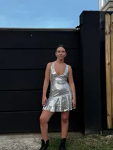 Vestido corto de lentejuelas color verde oliva, con escote en V, breteles finos cruzados en la espalda, cut-outs laterales y volado en el ruedo.