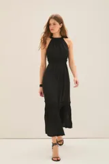 Vestido largo negro con escote halter con volados en cuello y fuelle con cinta interna para ajustar escote. Tiene volados y costuras elásticas en cintura y ruedo con volado.