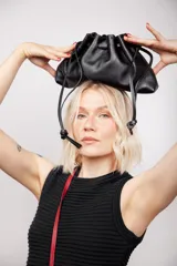 Bolso tipo sobre negro de cuero, con fruncido superior y cierre con cordones. Tiene correa larga desmontable y bolsillo interno con cierre.