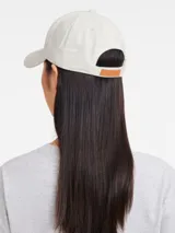 Gorra de béisbol color crema con logo bordado en verde en el frente.