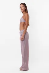 Pantalón de tela glitter color lila, de corte sastrero clásico y tiro medio. Tiene pasacinto, cierre con gancho metálico y cierre en cartera, bolsillos laterales diagonales y bolsillos traseros ribete falsos.