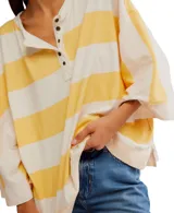 Remera de corte extragrande a rayas horizontales amarillas y blancas, confeccionada en jersey de peso medio, con textura suave y hombros caídos para un look relajado. Presenta un cierre frontal parcial con botón y terminaciones simples.