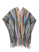 Capa tipo poncho de tejido de punto con diseño de zigzag multicolor en tonos amarillo, gris, negro y beige. Presenta cuello en V y flecos en el borde inferior.