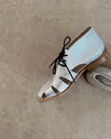 Zapato acordonado de cuero vacuno color marrón con aberturas laterales y cordones negros.
