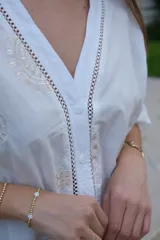 Blusa blanca de manga larga con elástico en puños, escote en pico y cierre frontal con botones. Detalles de bordados con hilado en tonalidad camel y acabado con entredoses a tono.