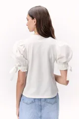 Remera blanca de algodón, con mangas abullonadas y detalles de lazo en los puños.