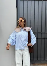Camisa celeste a rayas verticales blancas, de algodón, con cuello babero beige con volados, mangas largas abullonadas con puños elásticos y botones a contratono.