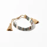 Pulsera tejida con cuentas de colores y detalles dorados, con cierre ajustable y borlas decorativas.