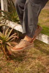 Zapatillas urbanas de cuero color taupe con detalles en terracota, cordones al tono y suela marrón.