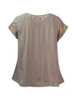 Blusa color taupe de mangas cortas con bordados florales en amarillo y fucsia. Tiene escote redondo con lazo y borlas amarillas.