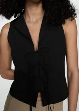 Blusa negra sin mangas con cuello camisero y cierre de lazos en la parte delantera.