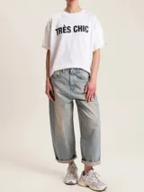 Remera blanca de algodón con cuello redondo y estampado negro con la frase "Très Chic" en el frente.