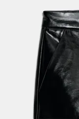 Shorts negros de tiro bajo con acabado brillante que simula cuero, cierre frontal con cremallera y gancho metálico, y bolsillos delanteros.