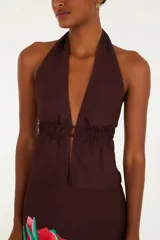 Top corto marrón con escote halter en V pronunciado y frunce bajo el busto. Presenta ajuste en la espalda y detalle de rosas que aporta un acento distintivo.