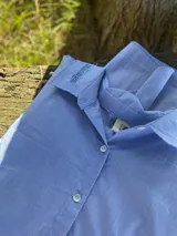 Camisa de corte oversize, color celeste con textura sutil. Presenta botones de nácar y bordado con la frase "alma oriental" en el cuello.