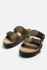 Sandalias planas color beige con doble tira ancha en el empeine y cierre con hebilla.