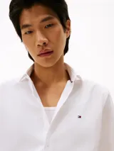 Camisa blanca de popelina de algodón regenerativo, corte slim fit, manga larga, cuello abotonado, cierre con botones y logo de Tommy Hilfiger bordado en el pecho.