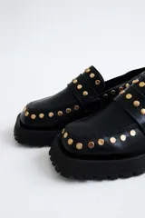 Mocasines de cuero color burdeos, adornados con tachas doradas, con suela gruesa.