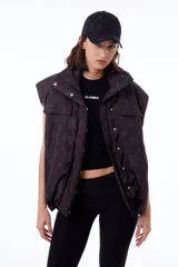 Chaleco negro con estampado de logos, cuello alto, cierre frontal con cremallera y broches a presión ocultos, bolsillos delanteros y cintura ajustable con cordón elástico. Interior de tafeta relleno de guata.