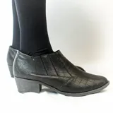 Bota de caña baja negra con textura de cocodrilo, elásticos laterales y tacón cuadrado.