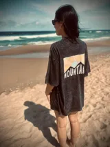 Remera negra con efecto gastado, corte holgado y estampa en la espalda con montañas y la palabra "Mountain" en blanco.