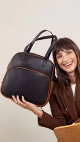 Mochila negra con detalles en marrón, con doble asa corta y correa larga desmontable.