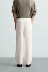 Pantalón de vestir color blanco hueso, de corte recto y tiro medio, con cintura elástica y cierre frontal de botón y cremallera. Presenta bolsillos frontales y bolsillos traseros de vivo.