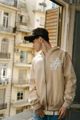 Hoodie con cierre frontal de algodón color crema con lavado acid wash. Presenta un logo estilizado en el pecho y estampados gráficos con caracteres orientales en ambas mangas.