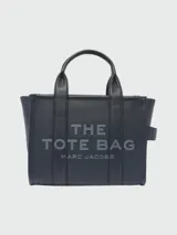 Bolso tote pequeño de cuero texturizado color gris con doble asa corta superior y correa larga extraíble y ajustable para llevar al hombro. Estampado frontal con el texto "The Tote Bag" y el nombre de la marca.