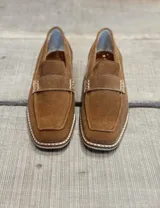 Mocasín de gamuza color marrón claro con detalle de hebilla y suela clara.