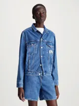 Campera de jean azul medio de corte clásico, con cuello en punta, bolsillos de parche en el pecho, bolsillos de hendidura en la cintura, botones metálicos de la marca y logo de Calvin Klein en el bolsillo del pecho.