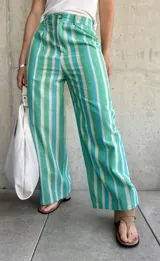 Pantalón de lino a rayas verticales en tonos verde, celeste y blanco, de corte holgado, con cierre y botón, y dos bolsillos laterales.