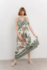 Vestido largo con estampado de hojas en tonos verdes y marrones sobre fondo blanco. Tiene breteles finos, escote en V y detalle de lazo en el frente. La falda es amplia y con vuelo.