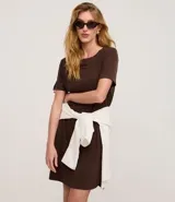 Vestido corto de mujer, estilo camiseta, color terracota/óxido, con escote redondo, mangas cortas y bolsillos laterales. El bajo es redondeado.