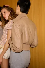 Chaqueta bomber de corte cropped confeccionada en material efecto piel color beige, con cuello subido, puños y cintura en rib elástico a tono, cierre frontal con cremallera y bolsillos laterales de vivo.