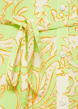 Vestido corto con estampado floral en tonos verde, amarillo y naranja. Tiene escote en V, mangas 3/4 con puños elásticos, cierre frontal con botones y lazo en la cintura.