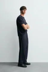 Pantalón de denim azul oscuro, corte wide fit, largo cropped, con pliegues frontales, bolsillos laterales y traseros asimétricos. Cierre frontal con cremallera y gancho metálico oculto.