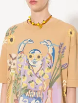 Remera color beige con estampado de figura humana con flores y objetos decorativos.