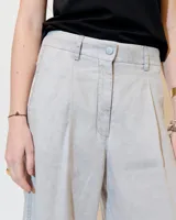 Pantalón gris de lino, de pierna ancha con pinzas, tiro medio, bolsillos laterales inclinados, raya de aplomo y bolsillos traseros ojal y con tapa. Tiene cierre y botón en la cartera y cintura interna prearmada.