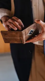 Billetera marrón de símil cuero con detalle bordado al frente. Interior con visor, doble repartición para billetes, tarjeteros y bolsillo.