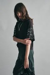 Remera marrón holgada de algodón con escote redondo y mangas al codo. Presenta bordados de canutillos y lentejuelas en las mangas.