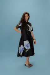 Vestido midi negro con estampado de flores y bichos en tonos celeste y blanco, con cuello camisero y botones frontales.